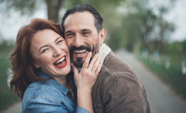 Laughing man and woman holding each other outdoors