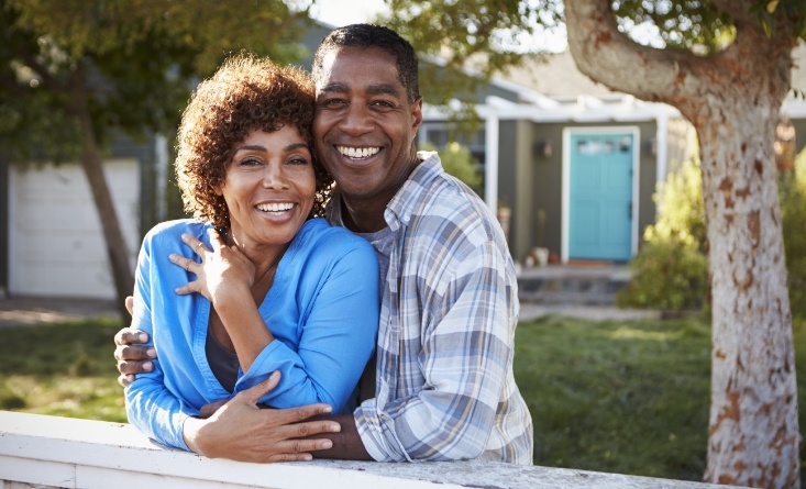 Smiling man and woman standing in their front yard