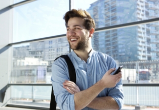 Smiling young man holding cell phone with city skyscrapers in background