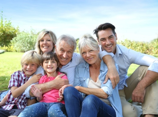 Three generations of smiling family sitting in grass