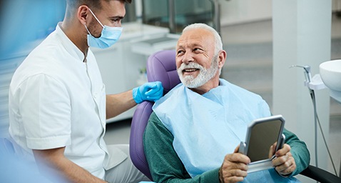 Senior patient looking at dentist while holding small mirror