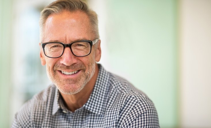 Older man in plaid shirt smiling with a same day dental crown