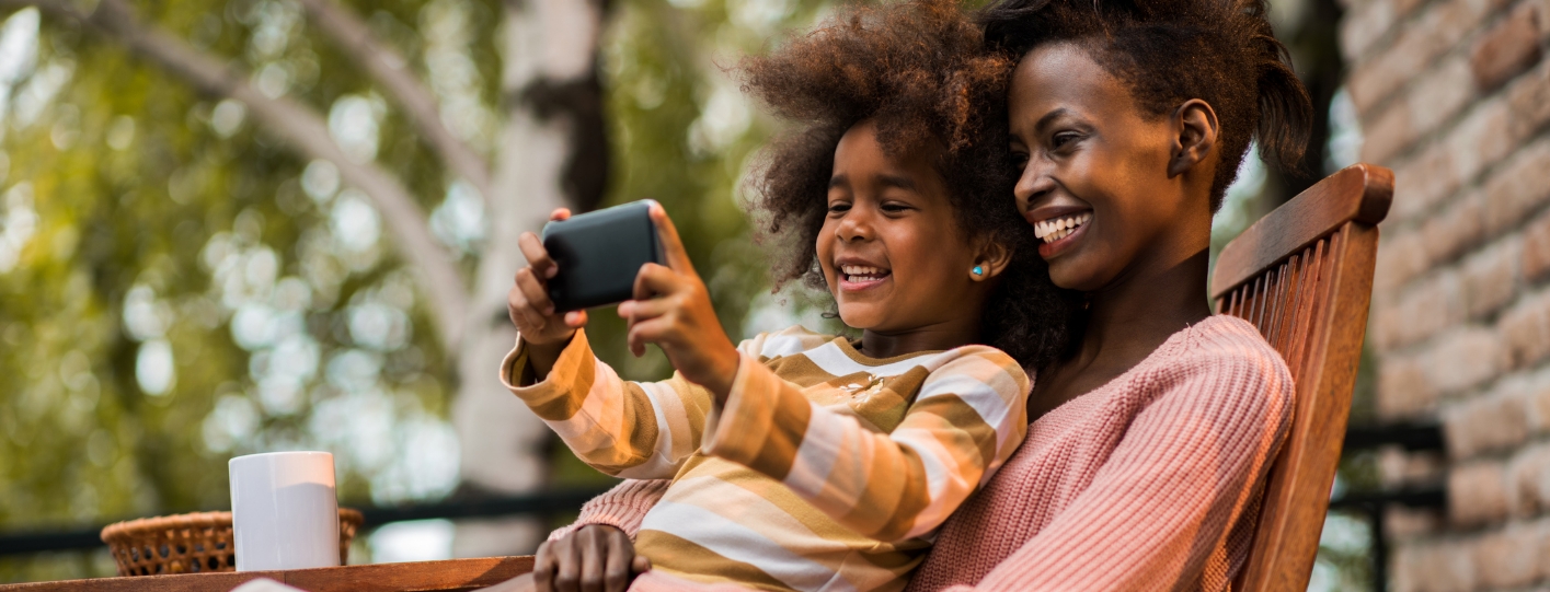 Little girl sitting in her mothers lap looking at phone