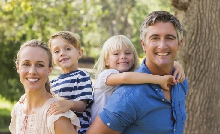 Family of four smiling outdoors after receiving dental services in Longmeadow