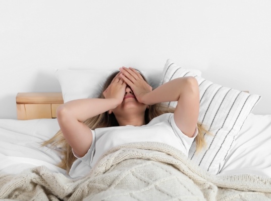 Woman lying in bed with her hands over her face