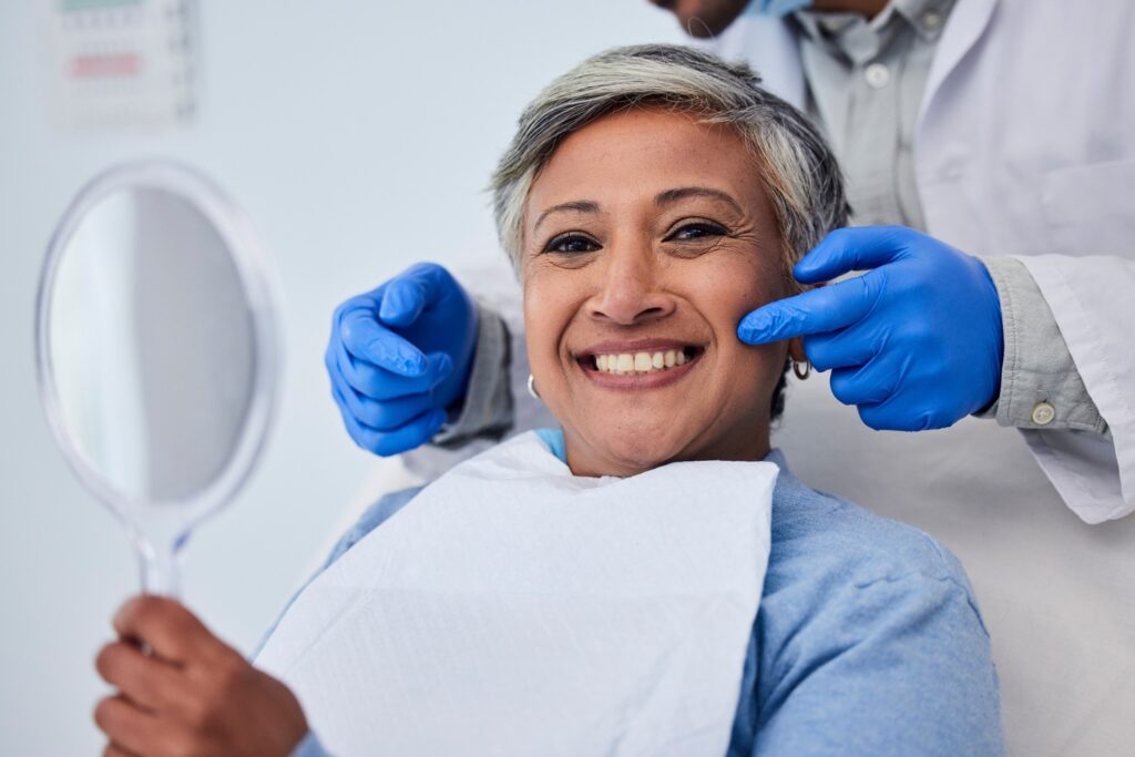 Woman smiling while holding handheld mirror at dental checkup