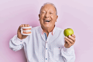 a patient with dentures smiling and holding an apple